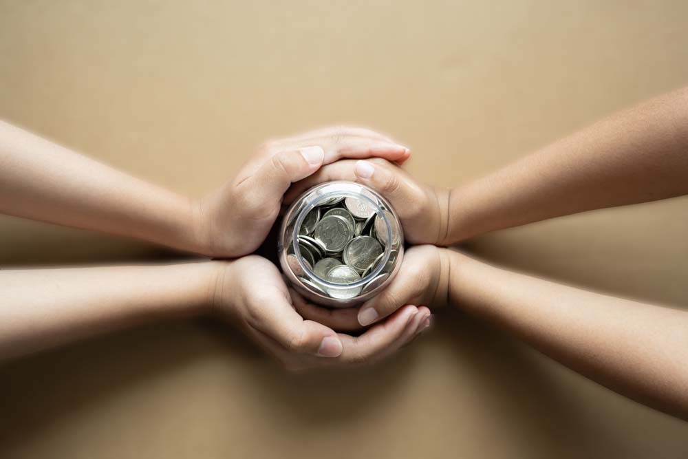 Kid hands holding coins in a jar together as saving concept for